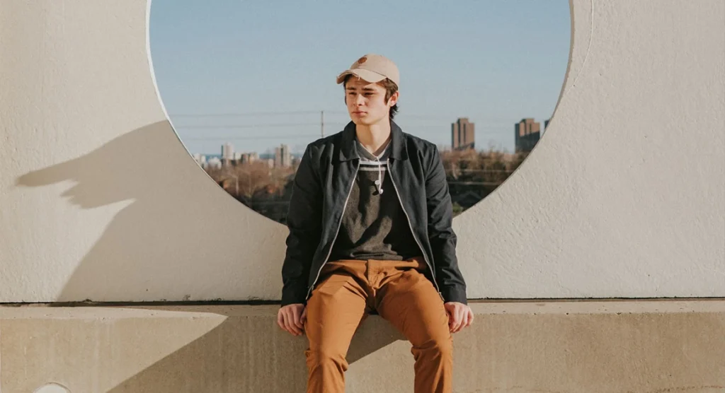 Young man in casual clothes sitting outdoors with urban background.