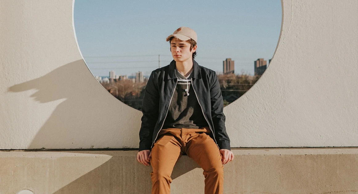 Young man in casual clothes sitting outdoors with urban background.