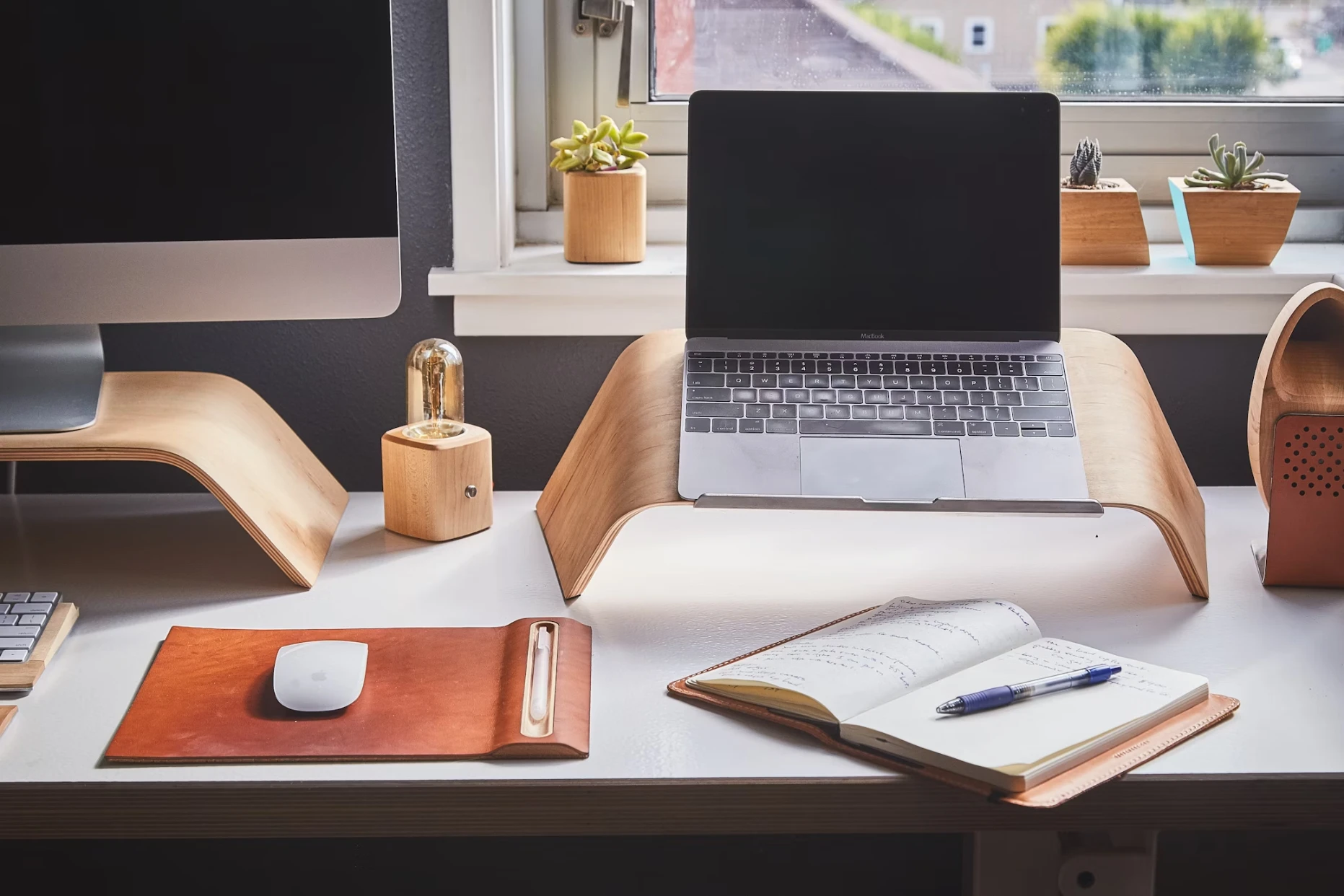 A tidy workspace with a laptop, notebook, and accessories on a white desk.
