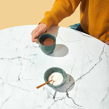 Hand pouring coffee into a cup on a marble table.