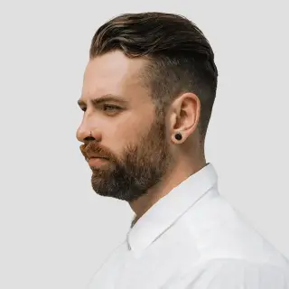Profile of a bearded man with a modern hairstyle and white shirt.