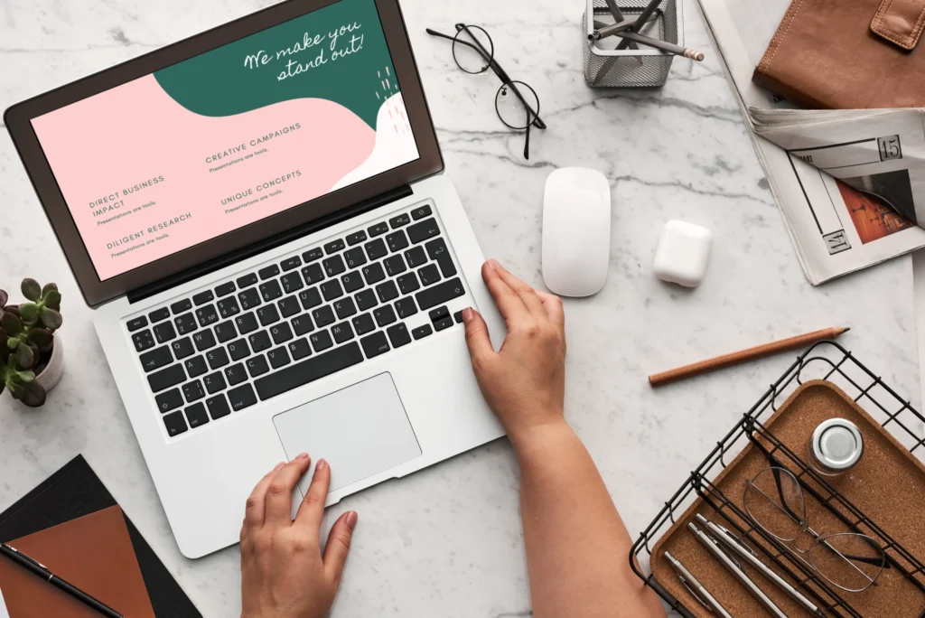 Person using a laptop with stylish pink and green cards nearby.