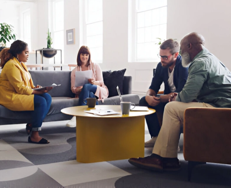 Four people engaged in a lively discussion around a yellow coffee table in a modern office.