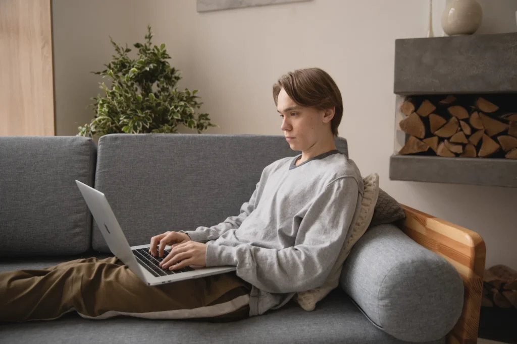 Young man working on a laptop while sitting on a couch.