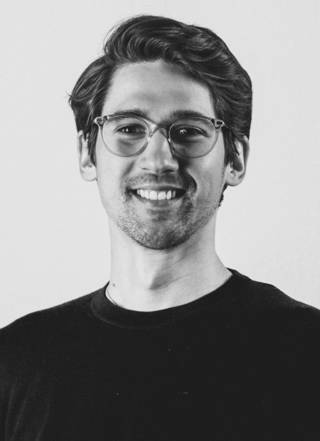 Young man smiling, wearing glasses and a black shirt.