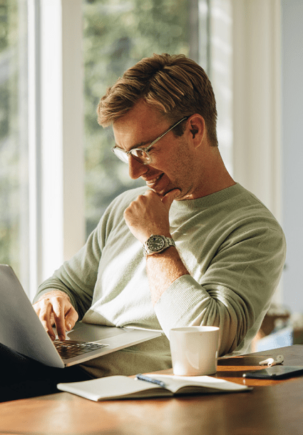 Man smiling while working on a laptop near a coffee cup.