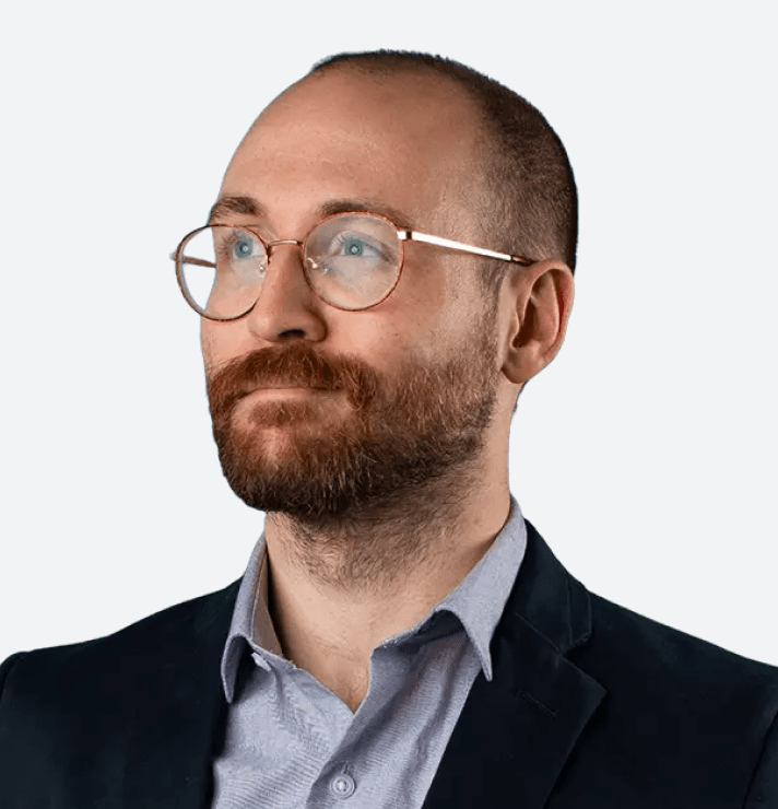 Professional man with glasses and beard in business attire looking thoughtfully.